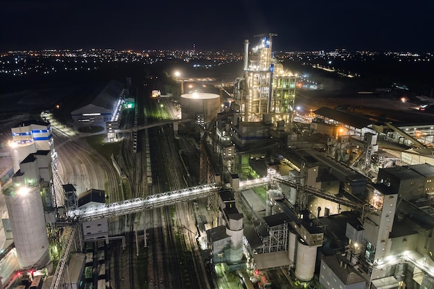 Aerial view of cement factory with high concrete plant structure and tower cranes at industrial production area at night Manufacture and global industry concept