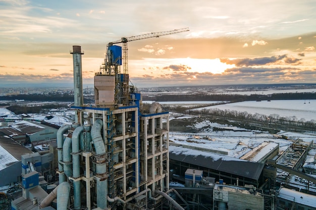 Aerial view of cement plant with high factory structure and tower crane at industrial production area at sunset.