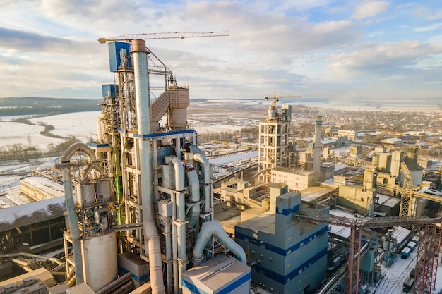 Вид с воздуха на цементный завод с высокой структурой завода и башенным краном на промышленной производственной площадке.