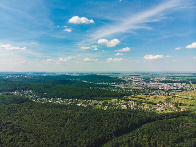 Вид с воздуха на город в центре зеленого леса. голубое небо с белыми облаками