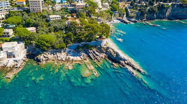 Aerial view on the city with colorful houses located on the rocky coast of ligurian sea, Camogli near Genoa, Italy. Rocky Coastline is washed by turquoise blue water.