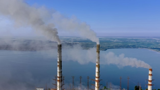 Aerial view of coal power plant high pipes with black smoke moving up polluting atmosphere at sunrise.