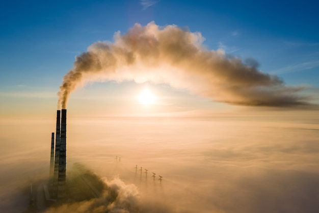 Vista aerea dei tubi alti della centrale elettrica del carbone con fumo nero che si alza atmosfera inquinante al tramonto.