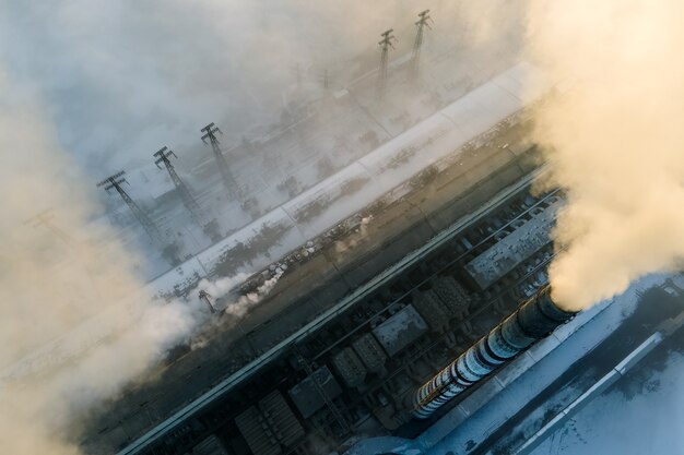 Вид с воздуха на высокие трубы угольной электростанции с черным дымом, движущимся вверх, загрязняя атмосферу на закате.
