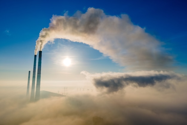 日没時に汚染された雰囲気を上昇する黒い煙のある石炭火力発電所のハイパイプの航空写真。