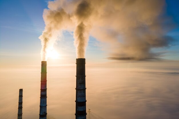 Vista aerea dei tubi alti della centrale elettrica del carbone con fumo nero che si alza atmosfera inquinante al tramonto.