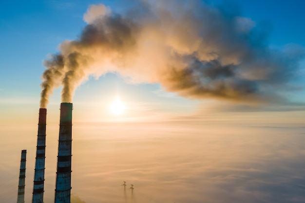 Вид с воздуха на высокие трубы угольной электростанции с черным дымом, поднимающимся вверх, загрязняя атмосферу на закате.