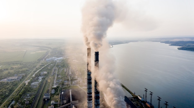 Vista aerea dei tubi alti della centrale elettrica del carbone con fumo nero che si alza atmosfera inquinante al tramonto.