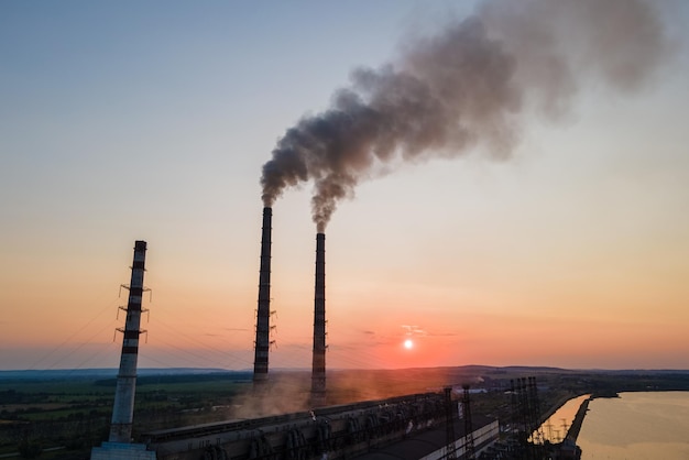 Вид с воздуха на высокие трубы угольной электростанции с черным дымом, движущимся вверх, загрязняя атмосферу на закате. Производство электроэнергии с использованием концепции ископаемого топлива