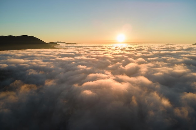 Вид с воздуха на красочный восход солнца над белым густым туманом с далекими темными силуэтами горных холмов на горизонте