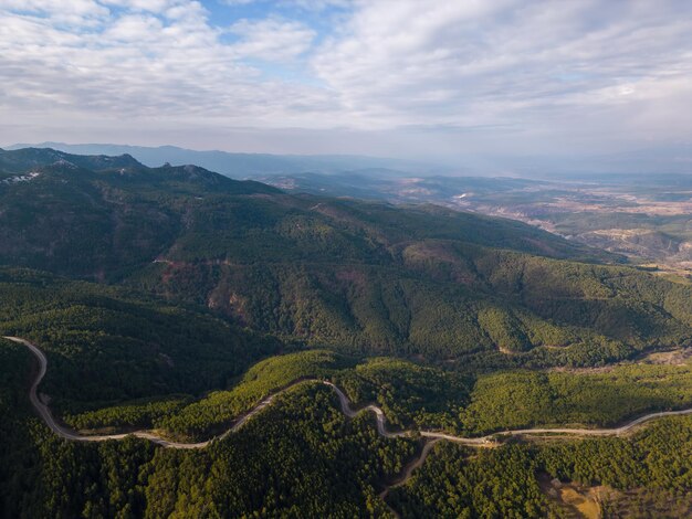 Вид с воздуха на сельскую дорогу, проходящую через зеленый лес и горы