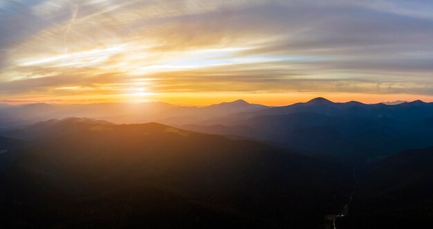 Aerial view of dark mountain hills with bright sunrays of setting sun at sunset Hazy peaks and misty valleys in evening