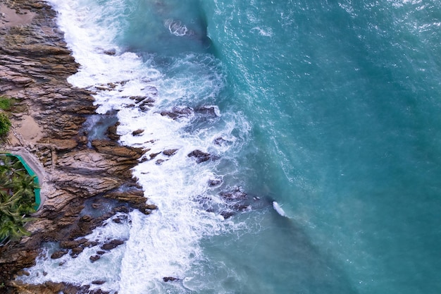 Aerial view Drone camera top down of seashore rocks in a blue ocean Turquoise sea surface Amazing sea waves crashing on rocks seascape High quality image of sea waves in Phuket Thailand