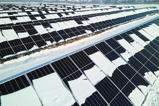 Воздушный вид электростанции с солнечными панелями, покрытыми снегом, тающий в конце зимы для производства чистой энергии Концепция низкой эффективности возобновляемой электроэнергии в северном регионе