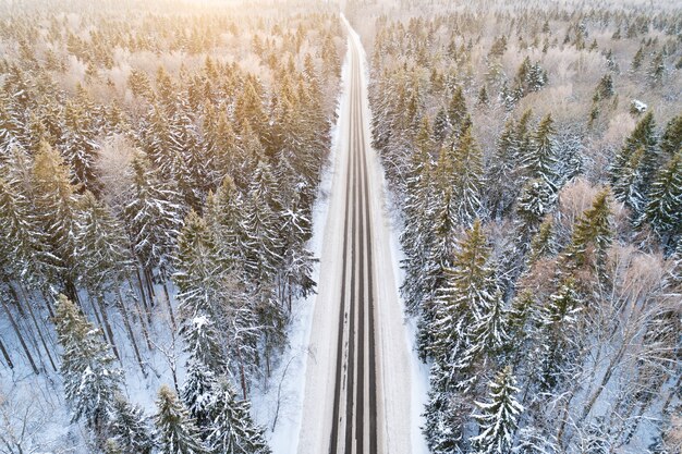 Вид с воздуха на пустую заснеженную дорогу в зимнем лесу