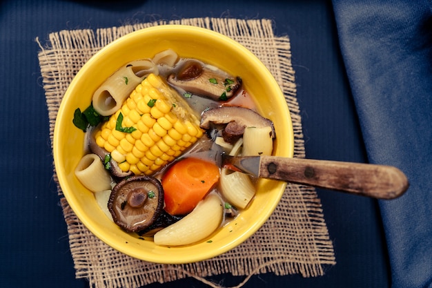 Aerial view of an exquisite homemade chicken, vegetable and mushroom soup with noodles and corn. Served in a bowl on a table with blue tablecloth. Natural and healthy food concept