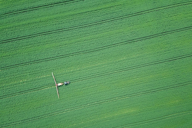 Aerial view Farm machinery spraying chemicals on the large green field, agricultural spring background.