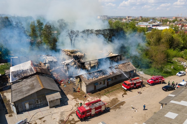 Aerial view of firefighters extinguishing ruined building on fire with collapsed roof and rising dark smoke.