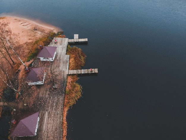 Aerial view of a fisherman with a fishing rod on the pier, lake shore, autumn forest. Finland.