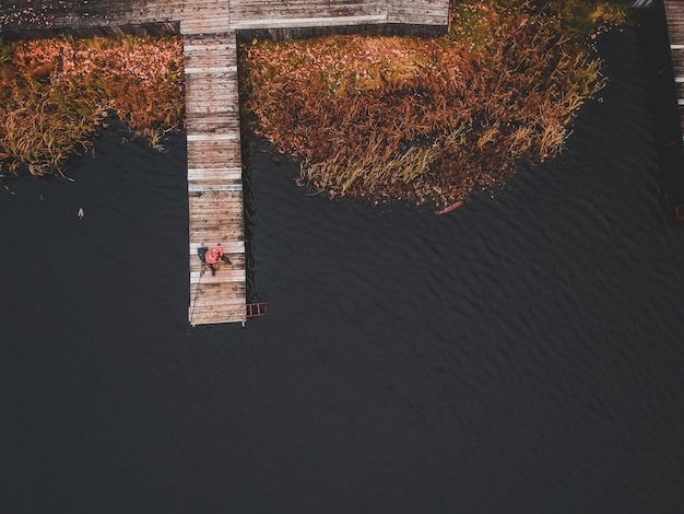 Aerial view of a fisherman with a fishing rod on the pier, lake shore, autumn forest. Finland.