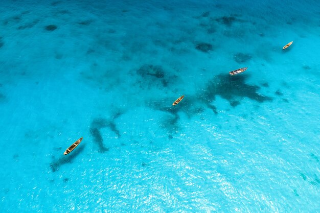 Aerial view of the fishing boats in clear blue water at sunny day in summer. Top view from above of boat, sandy beach. Indian ocean in Zanzibar, Africa. Landscape with canoe and clear sea. Travel