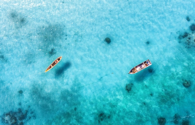 Aerial view of the fishing boats in clear blue water at sunny day in summer Top view from drone of boat sandy beach Indian ocean in Zanzibar Africa Landscape with sailboats clear sea Seascape