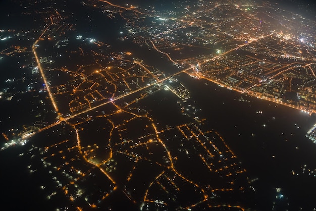 Aerial view from airplane window of buildings and bright illuminated streets in city residential area at night. Dark urban landscape at high altitude