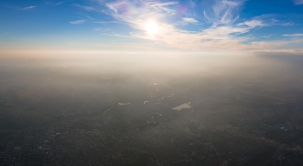 Aerial view from airplane window at high altitude of distant city covered with layer of thin misty smog and distant clouds in evening