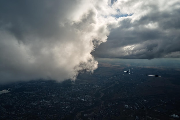 Aerial view from airplane window at high altitude of distant\
city covered with puffy cumulus clouds forming before\
rainstorm