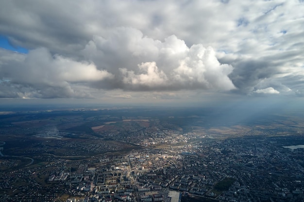 暴風雨の前に形成されるふくらんでいる積雲で覆われた遠方の都市の高高度での飛行機の窓からの空中写真