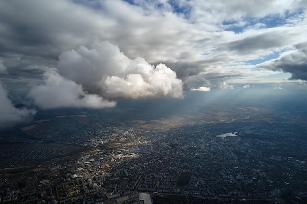 Aerial view from airplane window at high altitude of distant city covered with puffy cumulus clouds forming before rainstorm