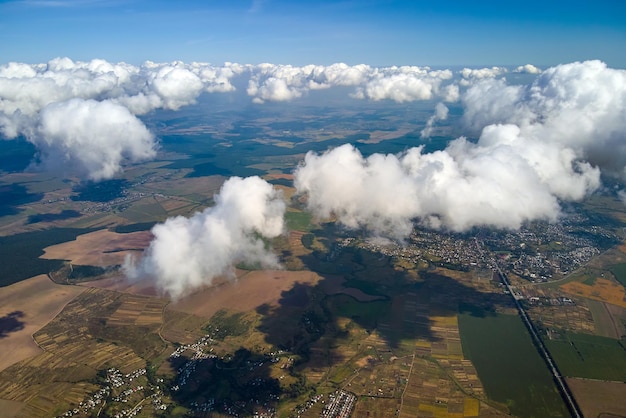 Aerial view from airplane window at high altitude of distant city covered with white puffy cumulus clouds.