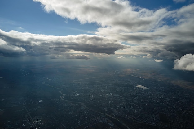 Aerial view from airplane window at high altitude of distant city covered with white puffy cumulus clouds