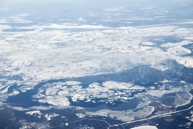 写真 雲の上の飛行機の窓から雪に覆われた川の野原や道路までの空撮