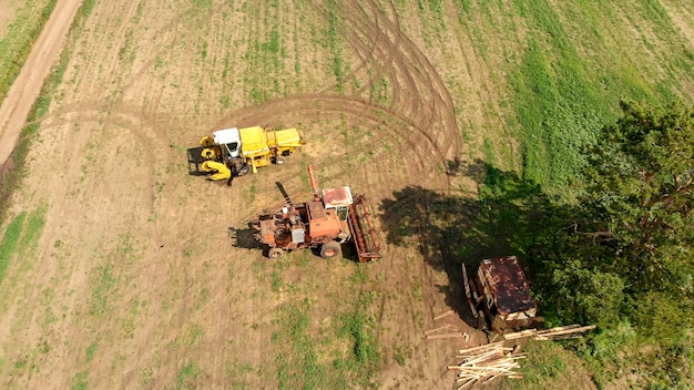 Aerial view from drone of two agriculture combine and harvesters, stand on wide brown field between lonely green tree