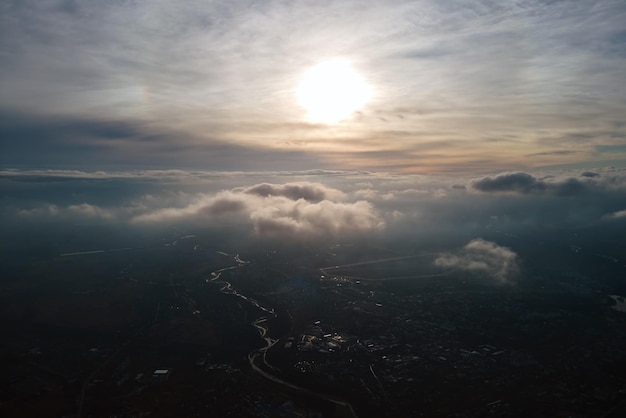 Aerial view from high altitude of distant city covered with\
puffy cumulus clouds flying by before rainstorm at sunset airplane\
point of view of landscape in cloudy weather