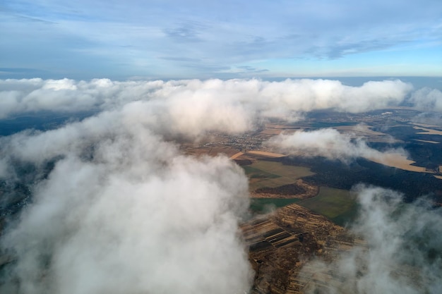 Aerial view from high altitude of distant city covered with\
puffy cumulus clouds forming before rainstorm airplane point of\
view of cloudy landscape