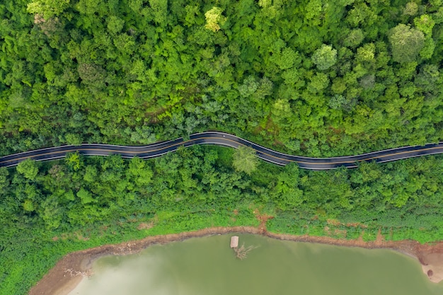 Aerial above view green mountain forest and river in the rain season and curved road on the hill connecting countryside