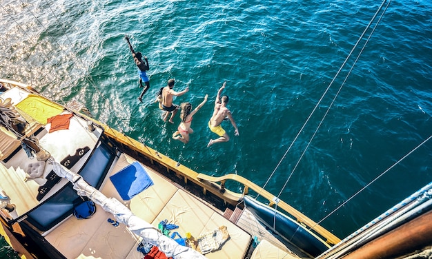 Aerial view of happy friends jumping from sailboat on ocean trip