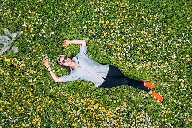 公園の野の花が咲く草の上に横たわる幸せな女性の空撮