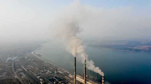 Aerial view of high chimney pipes with grey smoke from coal power plant.