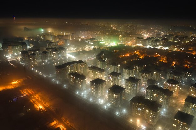 Aerial view of high rise apartment buildings and bright illuminated streets in city residential area at night. Dark urban landscape