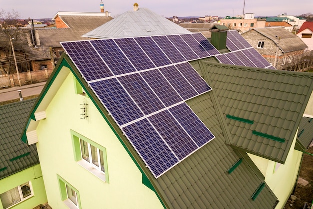 Aerial view of  house cottage with blue shiny solar photo voltaic panels system on the roof. Renewable ecological green energy production .