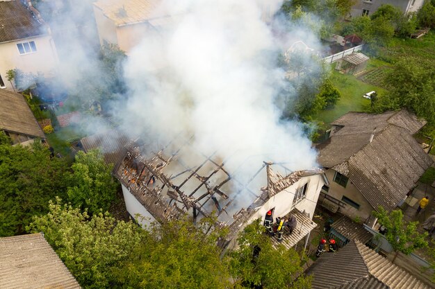 Aerial view of a house on fire with orange flames and white thick smoke.