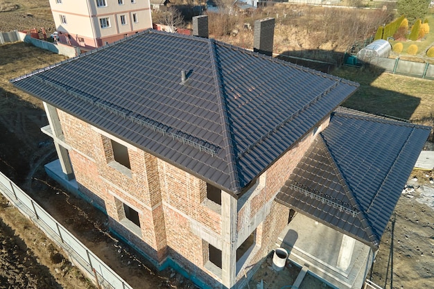 Aerial view of house roof top covered with ceramic shingles. Tiled covering of building under construction.