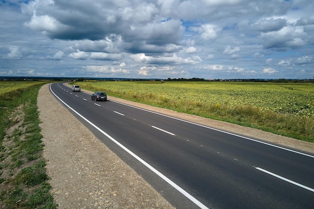 Aerial view of intercity road between green agricultural fields\
with fast driving cars top view from drone of highway traffic