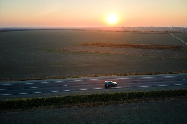 Aerial view of intercity road with blurred fast driving car at sunset. Top view from drone of highway traffic in evening.