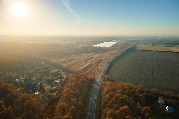 Aerial view of intercity road with fast driving cars between autumn forest trees at sunset Top view from drone of highway traffic in evening