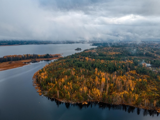 Aerial view on island with forest with green and yellow foliage. Low cloudy sky. Autumn landscape of Scandinavian nature. Viborg, Russia. Pure environment.