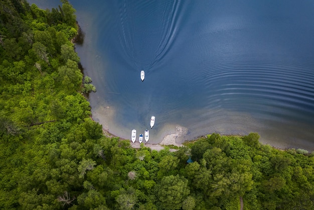 Вид с воздуха на озеро с лодками у берега и одной лодкой, плывущей к пирсу с зелеными деревьями